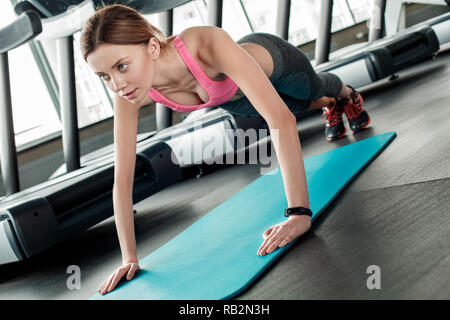 Young woman in gym healthy lifestyle standing on arms on yoga mat doing push ups concentrated side view Stock Photo