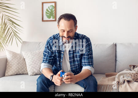 Man home alone sitting on sofa making combination on rubik's cube joyful Stock Photo