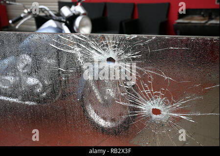 Cologne, Germany. 6th Jan 2019.  Bullet holes can be seen in a glass pane in front of an amusement arcade in the Buchheim district - a motorcycle stands in front of the building. Unknown persons had fired more than a dozen shots from a weapon on 04.01.2019. Photo: Henning Kaiser/dpa Credit: dpa picture alliance/Alamy Live News Stock Photo