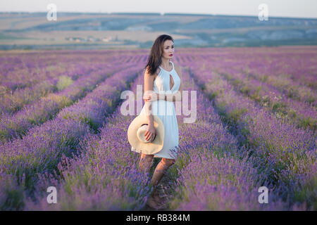 Young beautiful lady with lovely face walking on the lavender field on a weekend day in wonderful dresses and hats Stock Photo