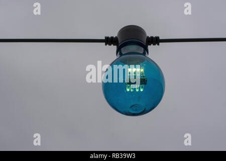 Blue color lightbulb on string against gray sky background Stock Photo