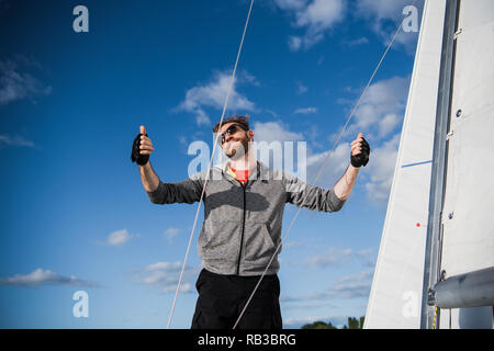 Nice happy bearded man sailor thumbing up and evincing positivity while at his yacht or boat on a river or sea. Stock Photo