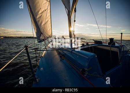 Sunset at the Sailboat deck while cruising sailing at opened sea or river. Yacht with full sails up at the end of windy day. Sailing theme - background. Yachting background design. Stock Photo