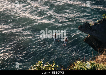 Two guys are surfing on surf boards in the ocean on Suluban Surf Beach Bali Indonesia. They are paddling outside on the blue water. Stock Photo