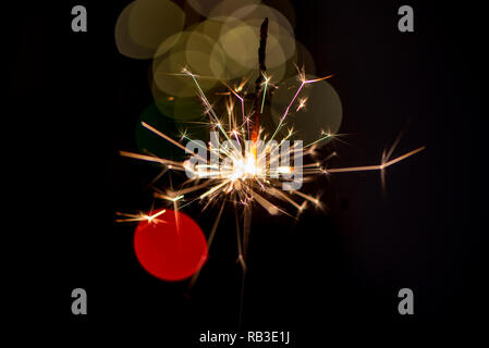 Single sparkler shining  in front of bokeh lights on a special day, isolated, close up. Sparkler in front of the bokeh effects Stock Photo