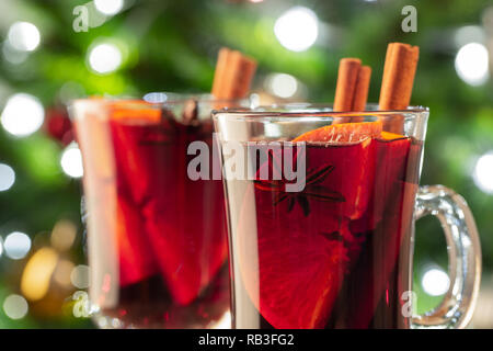 Two glass of christmas mulled wine or gluhwein with spices and orange slices on rustic table against the Christmas tree. Traditional drink on winter h Stock Photo