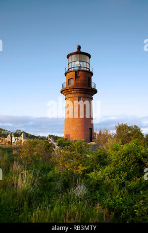 Light shines from the brick tower of Aquinnah lighthouse as the sun sets on a summer day on the island of Martha’s Vineyard. Stock Photo