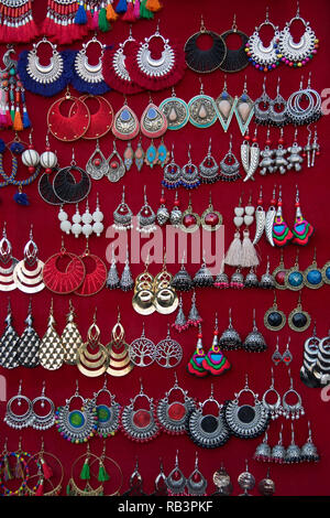 Closeup of different earings hanging on red fabric showcase Stock Photo