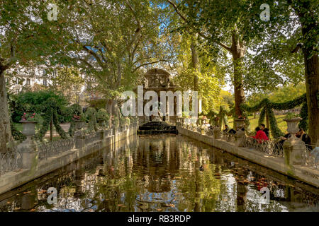 People sitting by the pond at The Medici Fountain or Fontaine de Medicis,a monumental fountain, on a summer's day in the Jardin du Luxembourg,Paris Stock Photo