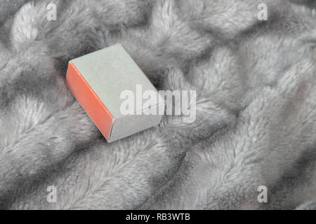 Small matchbox gift box with one orange side on the silver gray fluffy faux fur blanket background Stock Photo