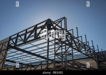 The steel framework of a prefabricated warehouse building against the sun and blue sky Stock Photo