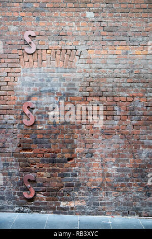 Old brick wall along a sidewalk with three S-shaped wall braces, vertical Stock Photo