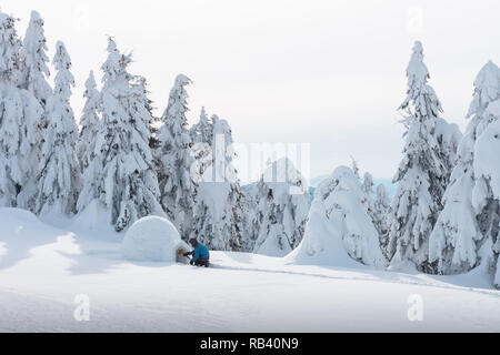 Man in blue jacket building igloo in the high mountain. Fantastic winter scene Stock Photo