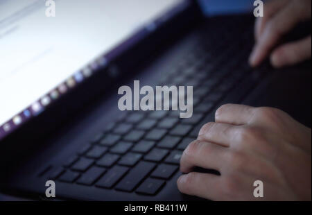 Woman working on laptop in home office hand on keyboard close up. in a dark environment. Stock Photo