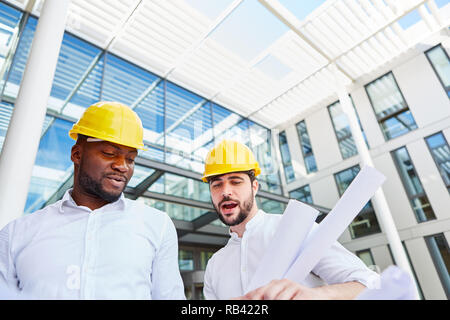 Two architects or construction manager with blueprint working in team in front of an office house Stock Photo
