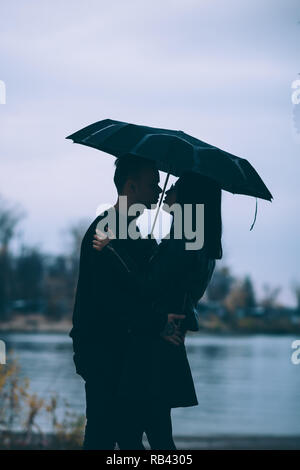 young couple standing under a dark umbrella. Stock Photo