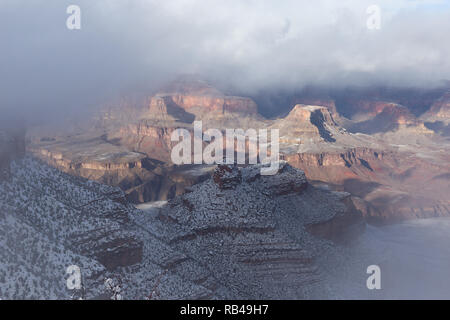 Sunlight peeks through the clouds as a winter snow storm begins to clear on the South Rim of the Grand Canyon in Grand Canyon National Park, Arizona, USA Stock Photo