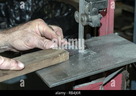 The metal worker carefully shapes a metal piece using a band saw for cutting. A bokeh background was captured. Stock Photo