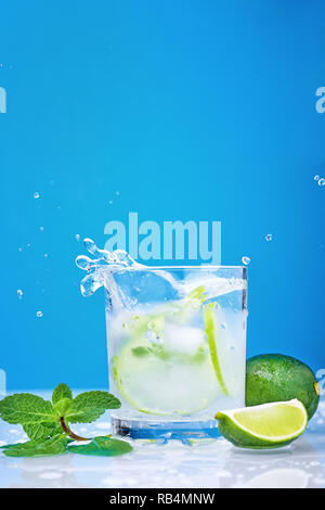 Splashing mojito cocktail with lime and fresh mint in glass on blue background Stock Photo