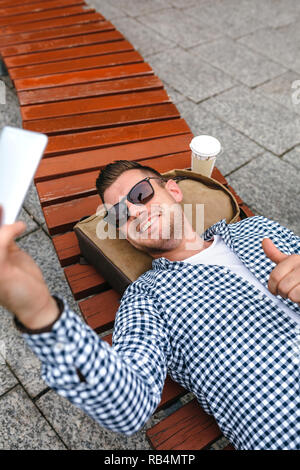 Man lying on a park bench making selfie with mobile Stock Photo