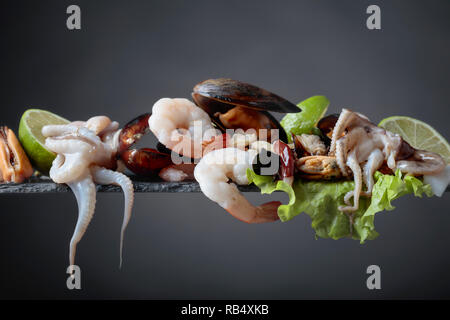 Mixed raw delicious seafood with lime slices on a dark background. Small octopuses, shrimps and mussels on a leaf of salad. Mediterranean kitchen, hea Stock Photo