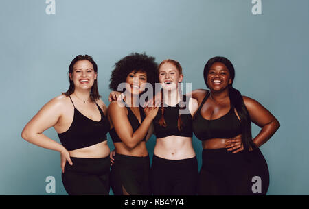 Portrait of group of women posing together in sportswear against a gray background. Multiracial females with different size standing together looking Stock Photo