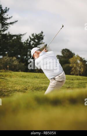 Professional senior golfer playing golf on the course. Man hitting the ball out of a sand bunker. Stock Photo