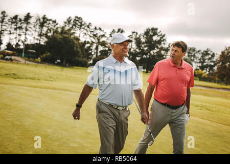 Two senior man playing golf are walking to the next hole. Professional golfers walking and talking on the golf course. Stock Photo