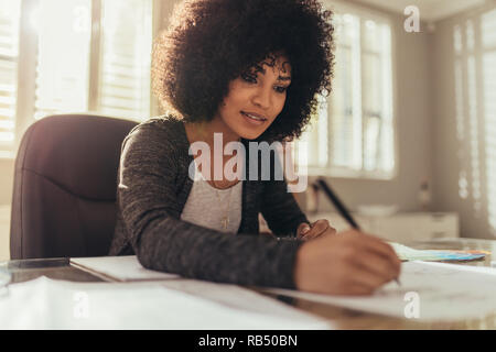 Concentrated young businesswoman working on blueprints in the office. African female architect working on new designs at her home office. Stock Photo