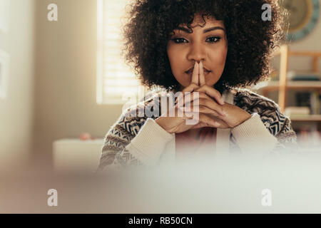 African woman with curly hair sitting at her desk and thinking. Portrait of thoughtful female worker at home office. Stock Photo