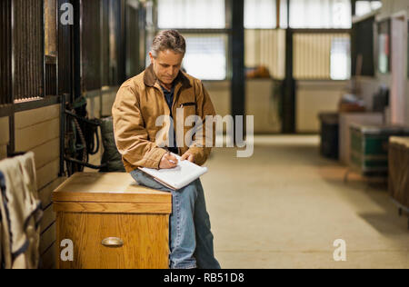 Focused mature man writing on a clipboard in a stable. Stock Photo