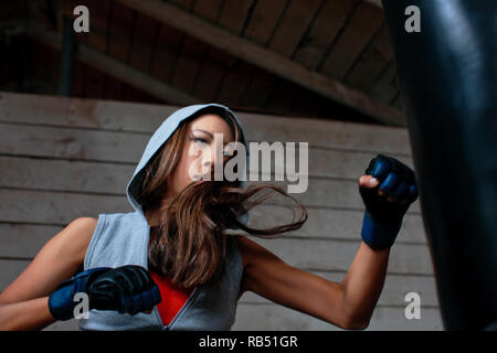 Tough young woman punching boxing bag. Stock Photo