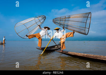 two fishermen in Inle Lake fishing in two boats in the traditional Burmese way with blue sky in the background Stock Photo