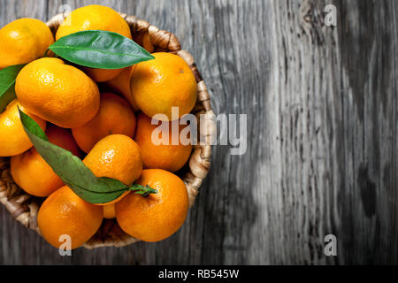 Tangerines with leaves in basket on rustic wooden background. Stock Photo