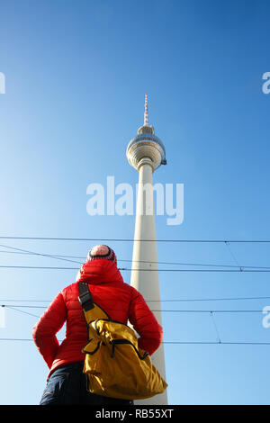 Tourist looking at the monumental TV Tower, Fernsehturm, dominating Berlin sky, Germany, from below. City sightseeing, tourism, monument, cityscape. Stock Photo