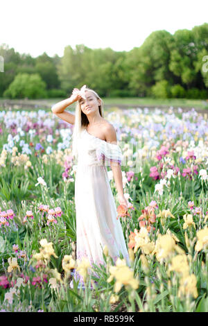 Young girl wearing white dress standing near irises on garden. Stock Photo