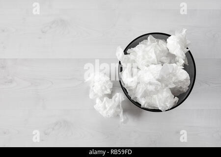 Black metal trash bin full of crumpled waste paper on white wooden floorboard. Top down view. Stock Photo