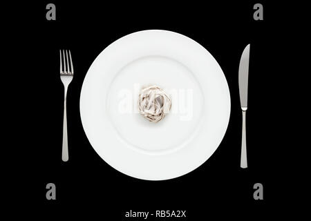 Small portion of tagliatelle pasta on round white plate with fork and knife on isolated black background. Concept of dieting and healthy eating. Stock Photo