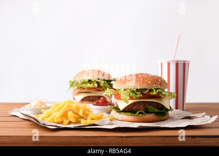 Two classic beef burger with cheese and tomatoes and onion and bacon accompanied by souces on wooden table with white backgorund. Front view. Horizont Stock Photo
