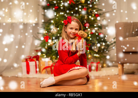 girl in red dress hugging teddy bear at home Stock Photo