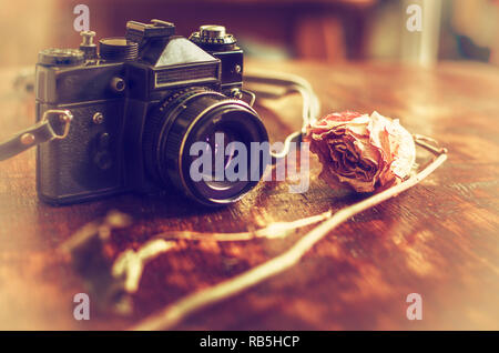 Retro photo camera and dry rose on a wooden table. Stock Photo