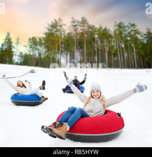 happy friends sliding down hill on snow tubes Stock Photo