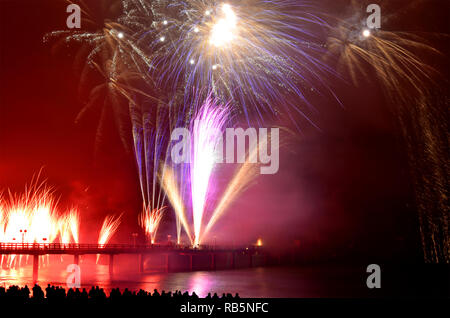 Colorful firework popping and lighting up the dark sky. Water reflection from coast. Stock Photo