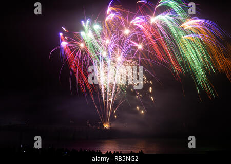 Colorful firework popping and lighting up the dark sky. Water reflection from coast. Stock Photo
