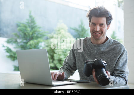 Man using laptop and holding digital camera Stock Photo