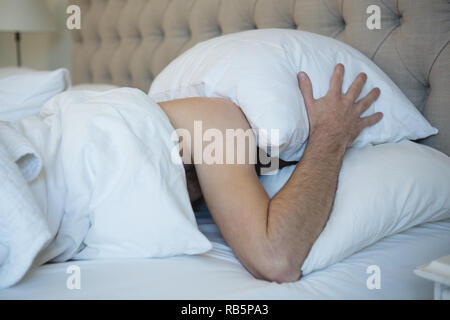 Man with pillow covering his face while sleeping in bedroom Stock Photo