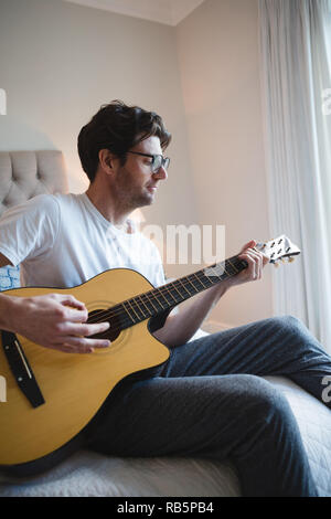 Man playing guitar in bedroom Stock Photo