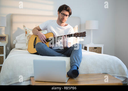 Man playing guitar in bedroom Stock Photo