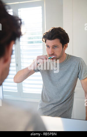 Man looking at mirror and brushing his teeth in bathroom Stock Photo