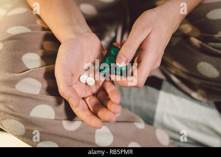 Subject medicine health and pharmaceuticals. Close-up macro young caucasian woman hands pulling out a green blister. Packing two white round pills in home clothes at home on the bed Stock Photo